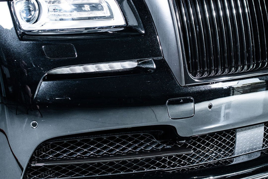 Close-up of a luxury black car's front grille and headlight detailing, showcasing sleek design and craftsmanship